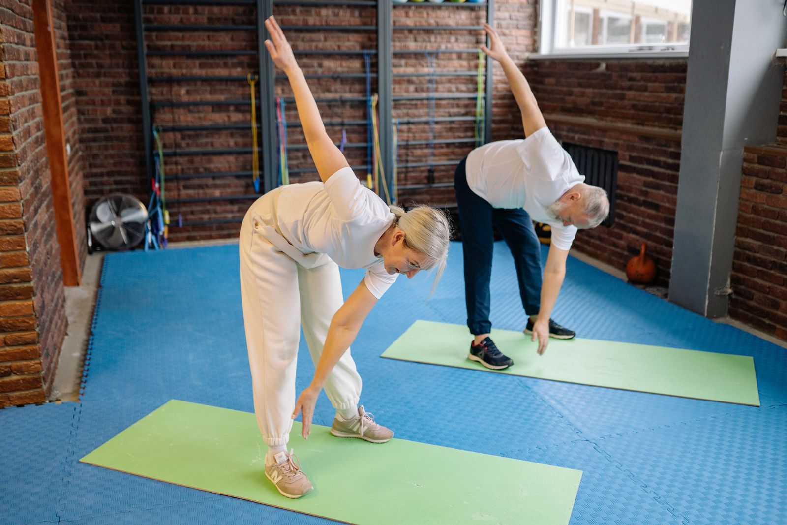 An older couple doing a side stretch on mats