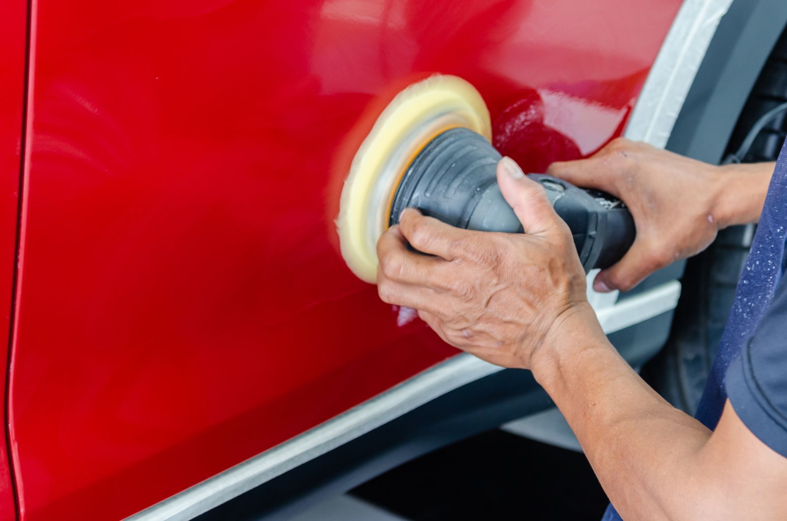 A polisher with a foam pad on red paint