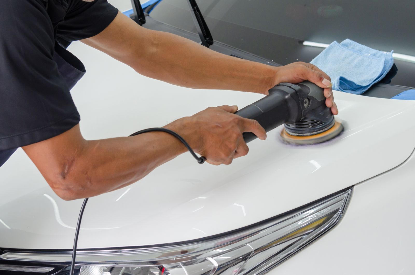 A detailer machine polishing the hood of a white car