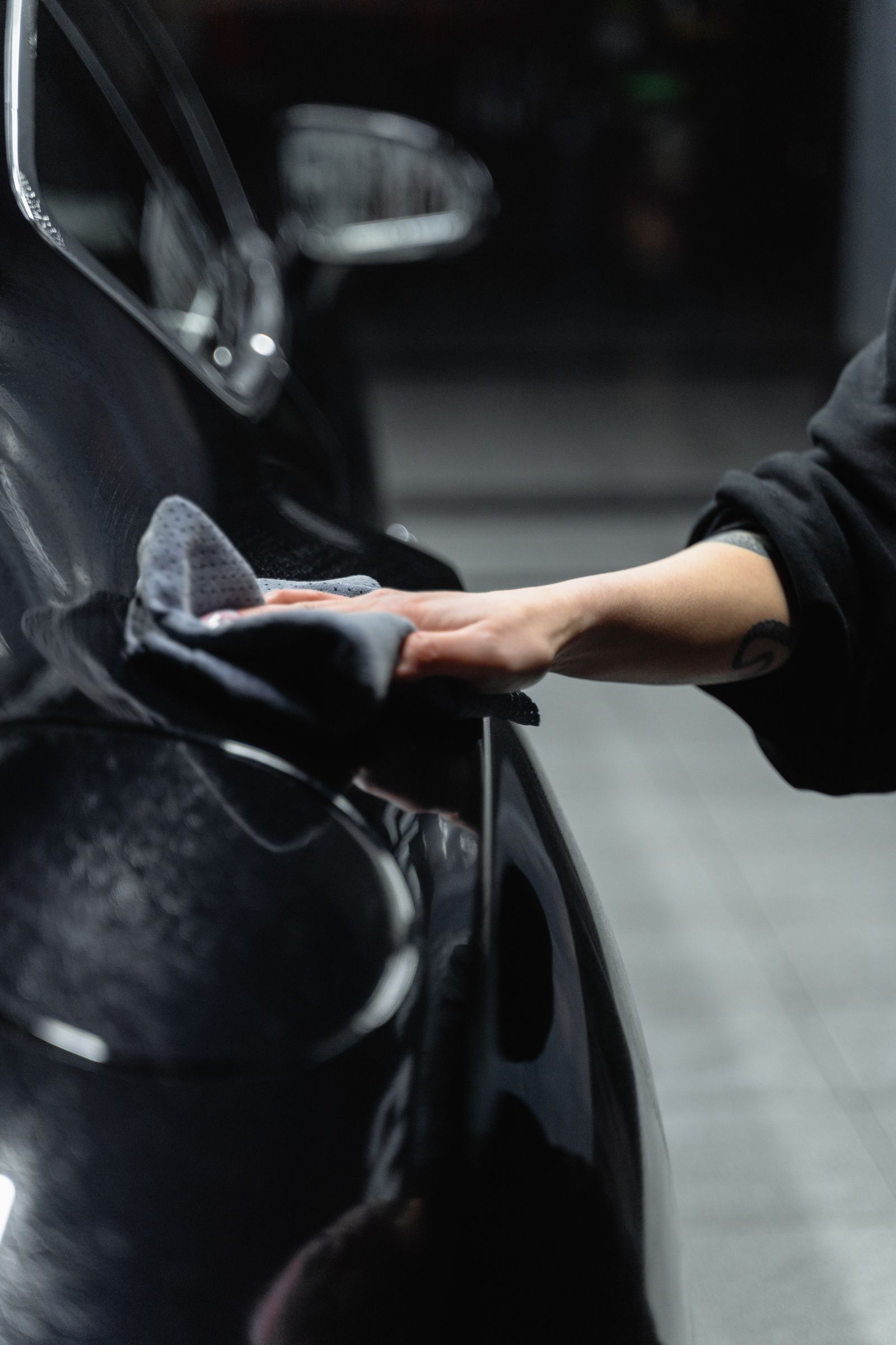 A gloved hand wiping a glossy black car panel with a microfibre cloth under studio lights