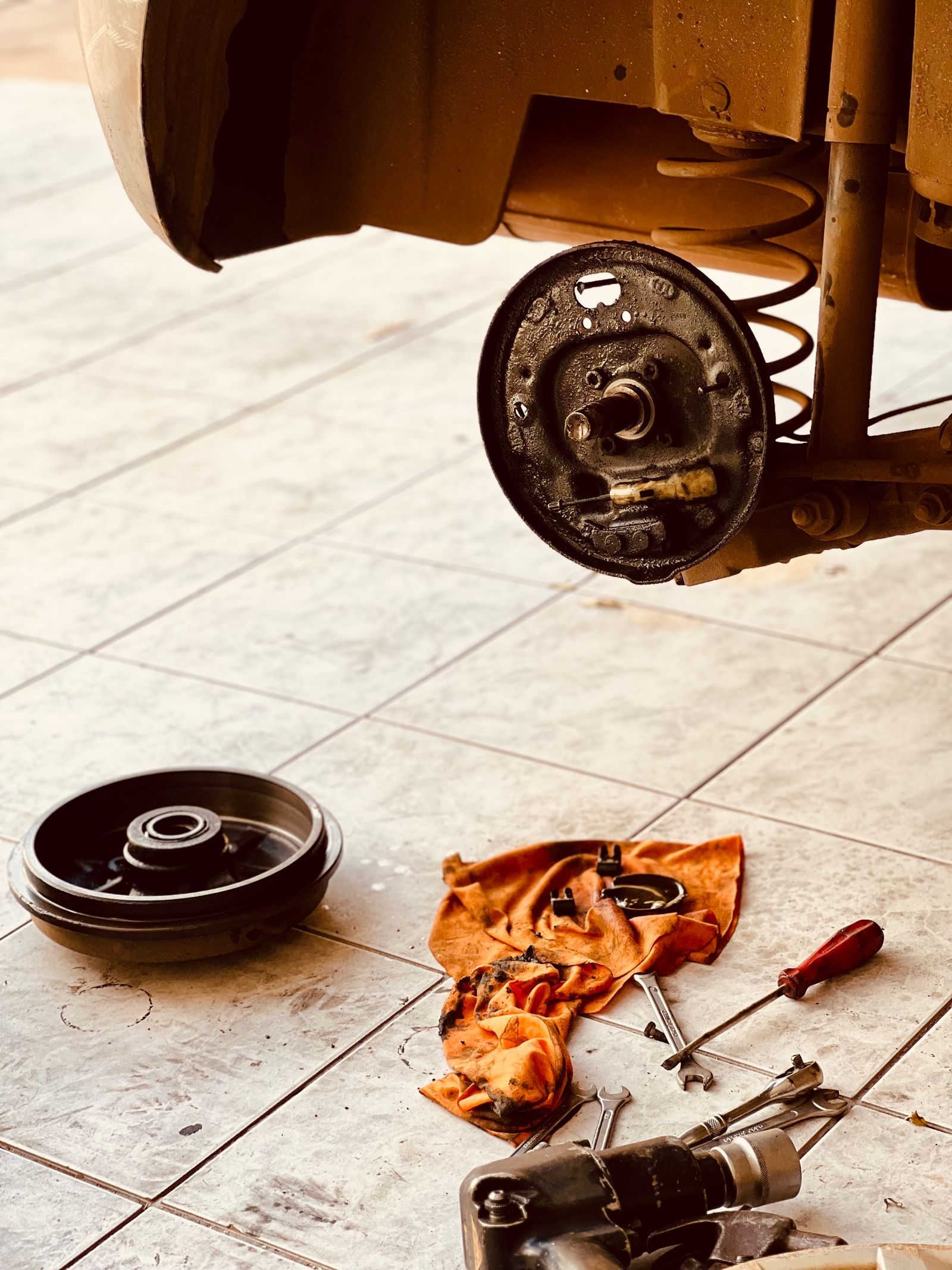 A drum brake taken apart on the shop floor beside a rag and screwdriver