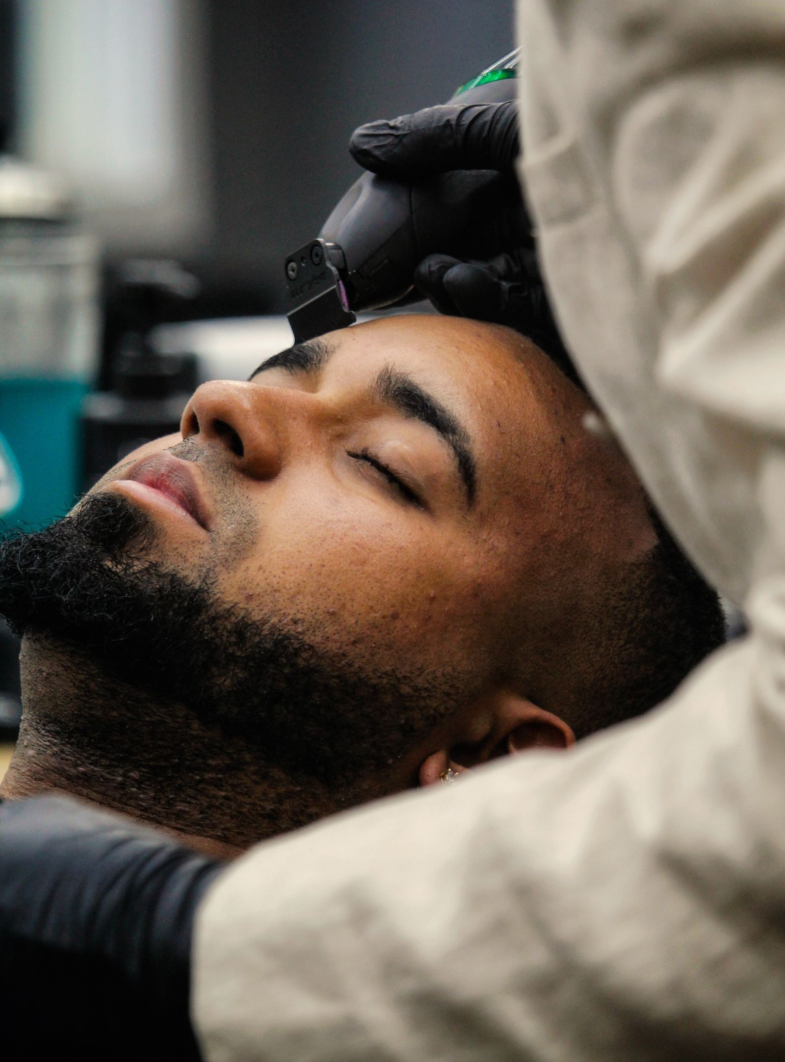 A client leaning back while a barber in gloves lines up his beard with a trimmer