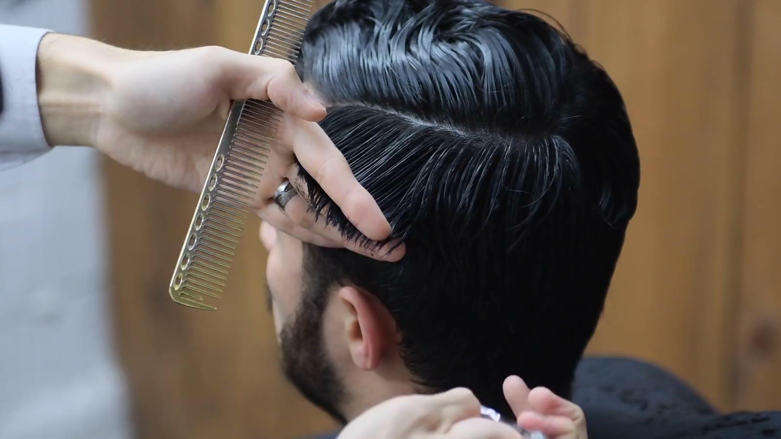 A barber cutting the side of a client's hair with scissors and a comb