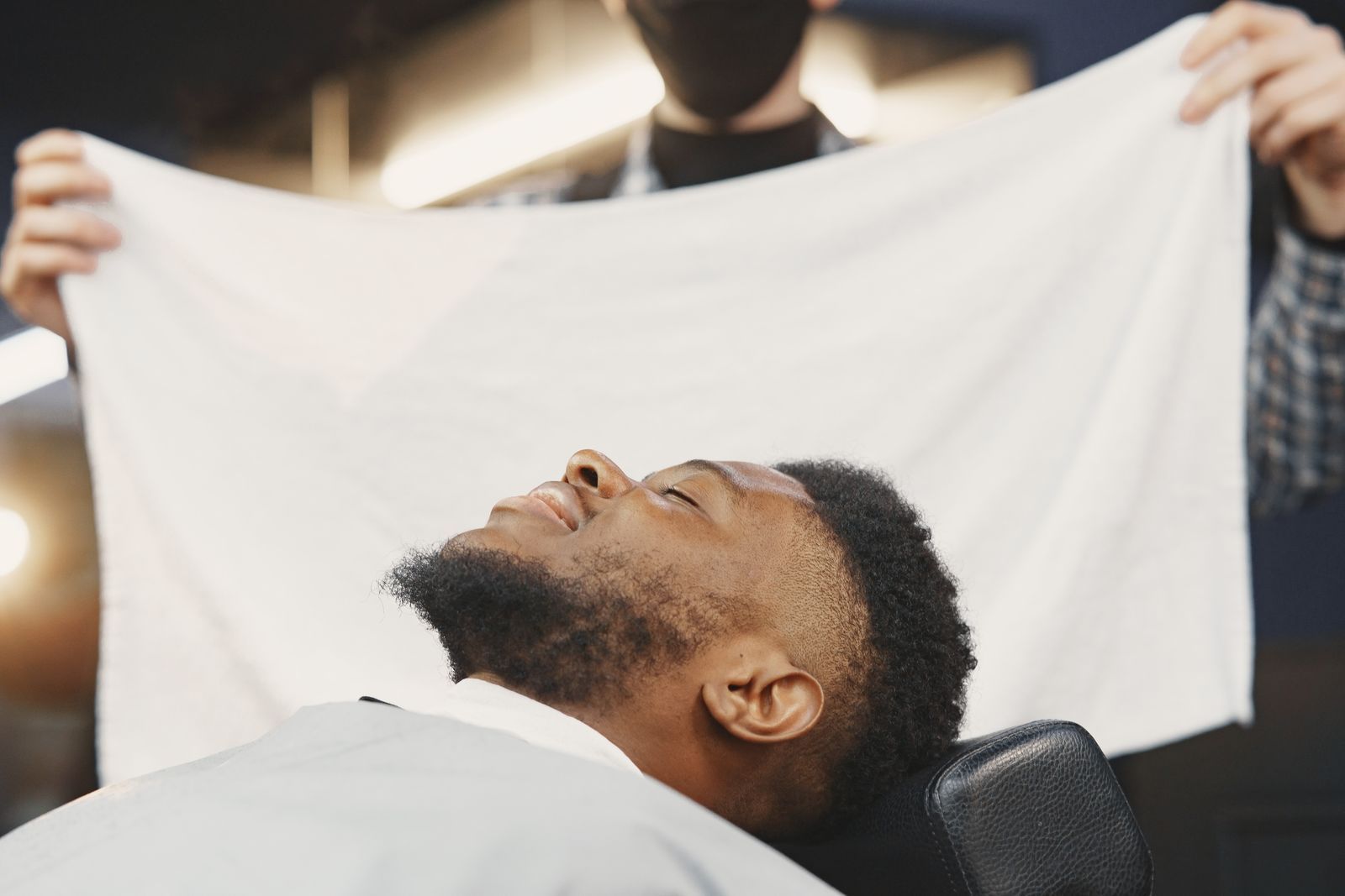 A client relaxing under a hot towel in the barber chair
