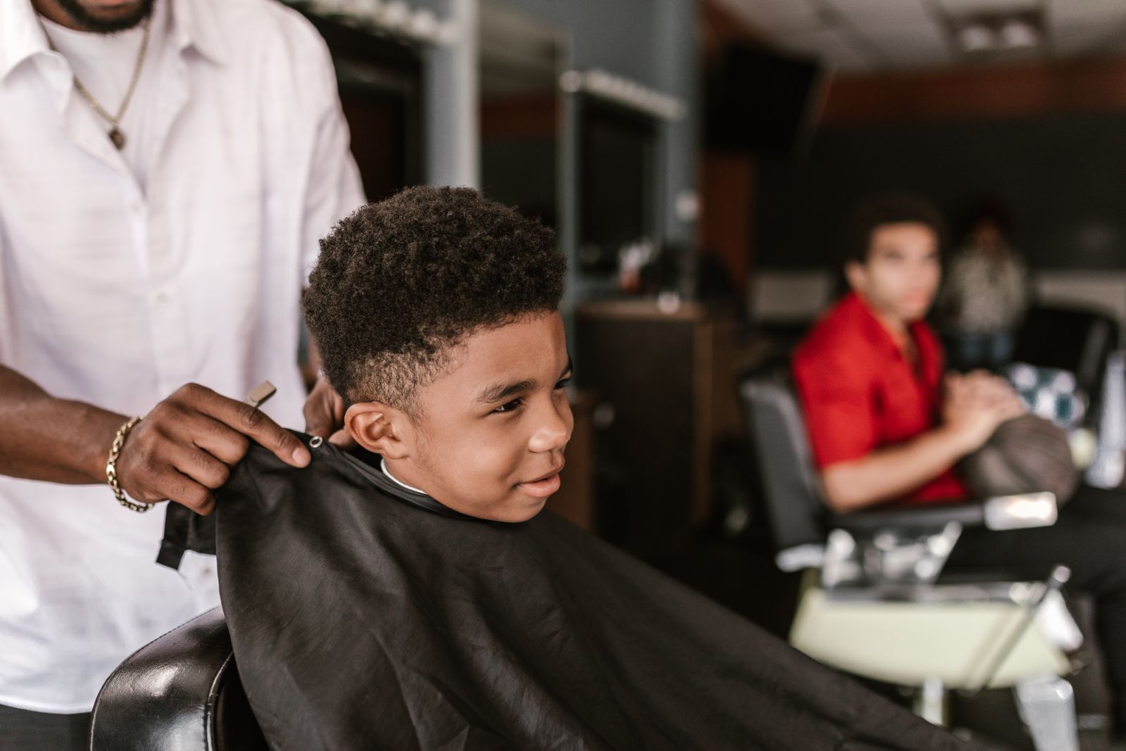 A smiling boy in a black cape as the barber fastens it