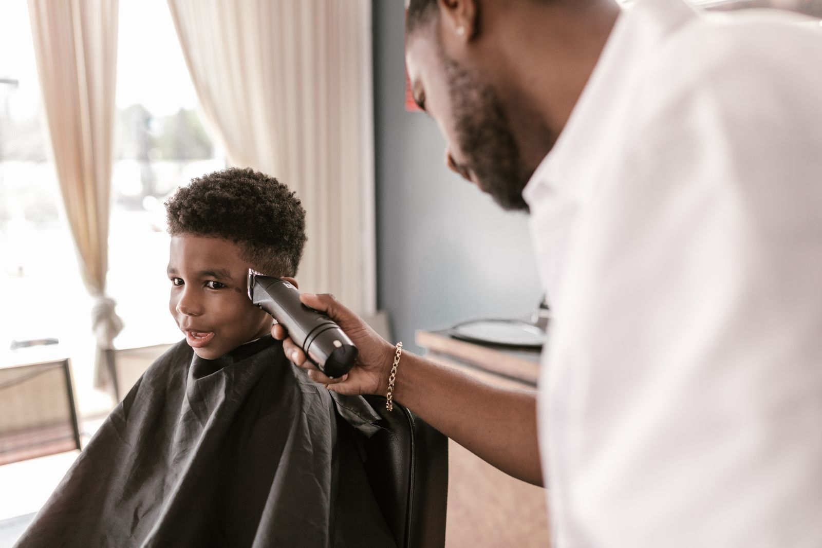 A boy grinning at the mirror as the barber trims the side of his hair