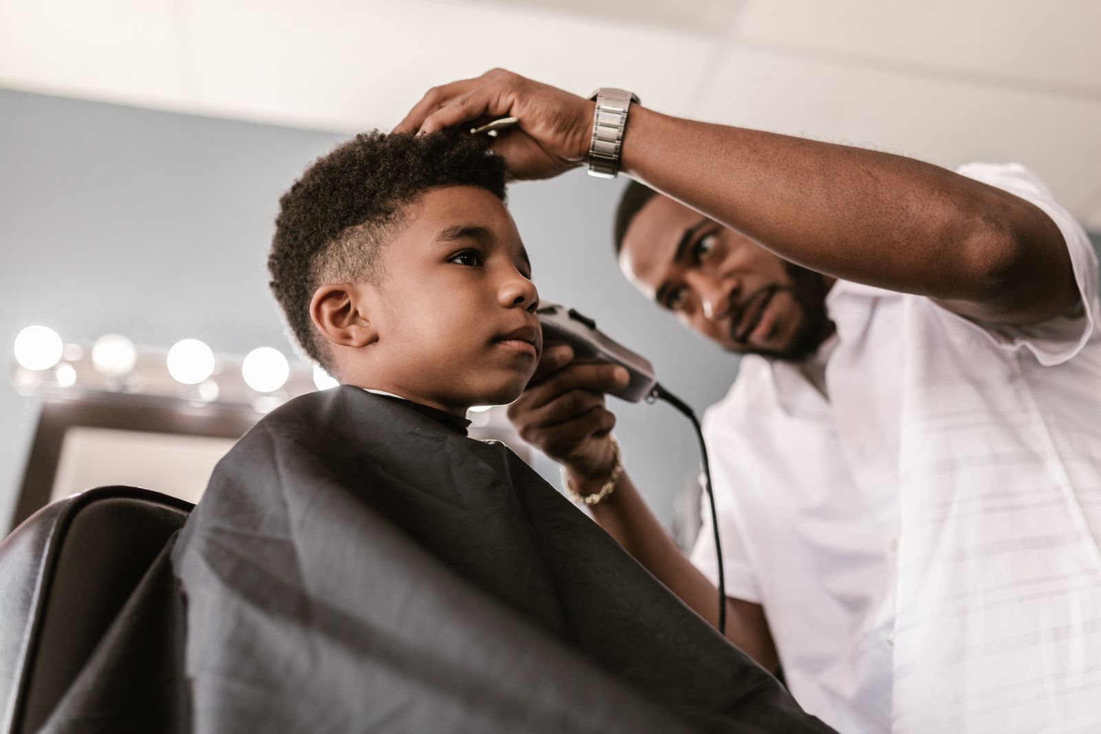 A barber trimming a young boy's hair with clippers while the boy sits still in the chair
