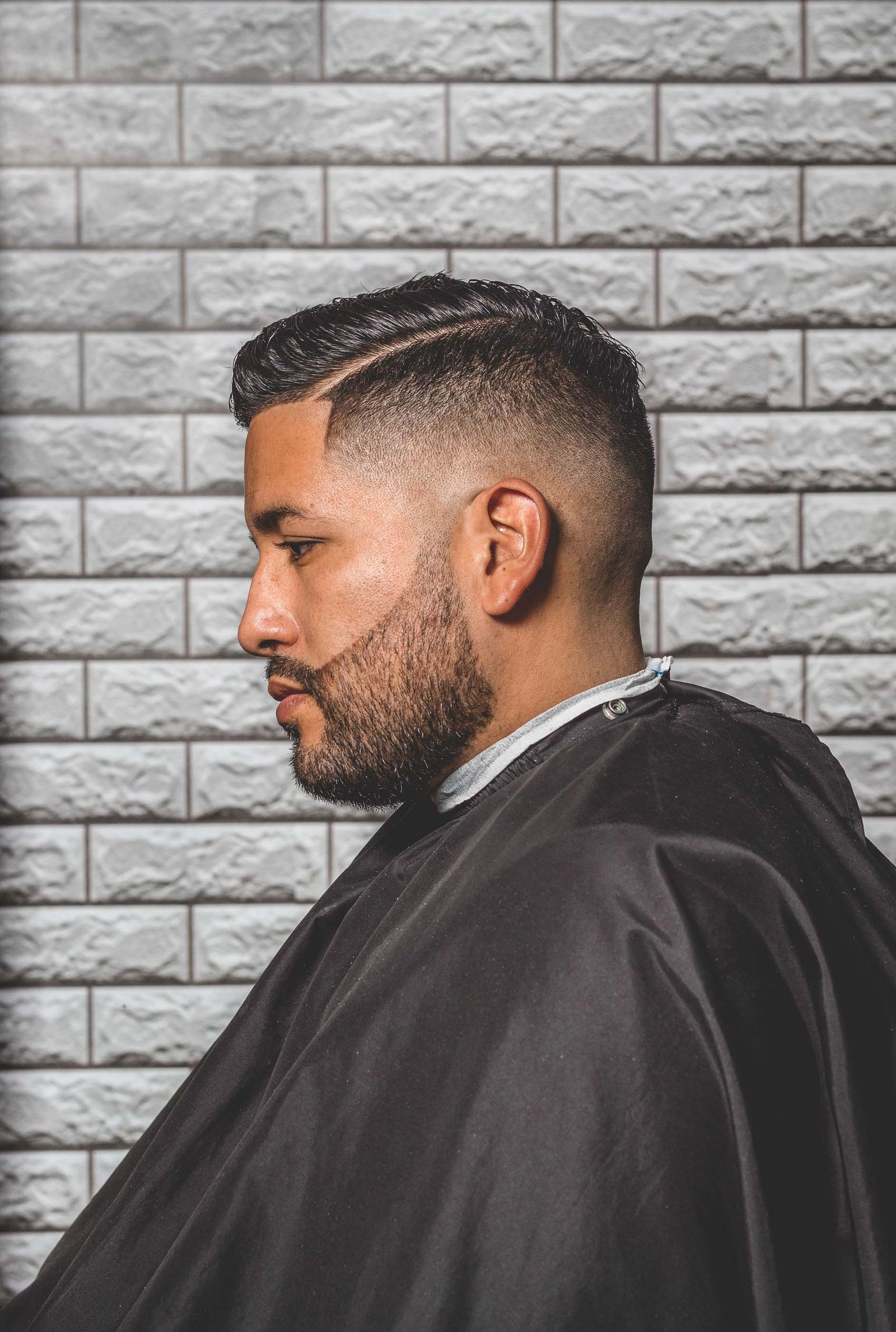 Side view of a slicked side part with a mid fade and full beard