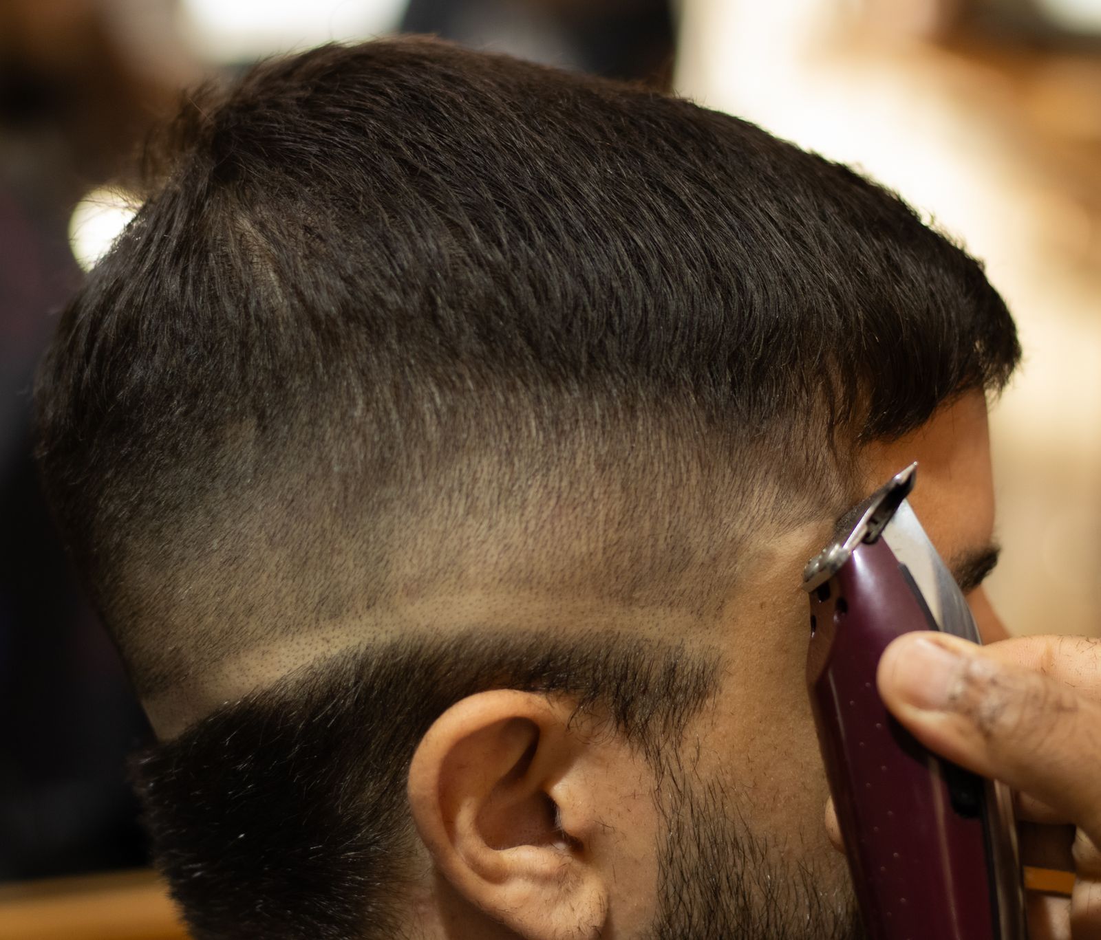 A barber taking a mid fade down to skin with clippers, with a sharp part line