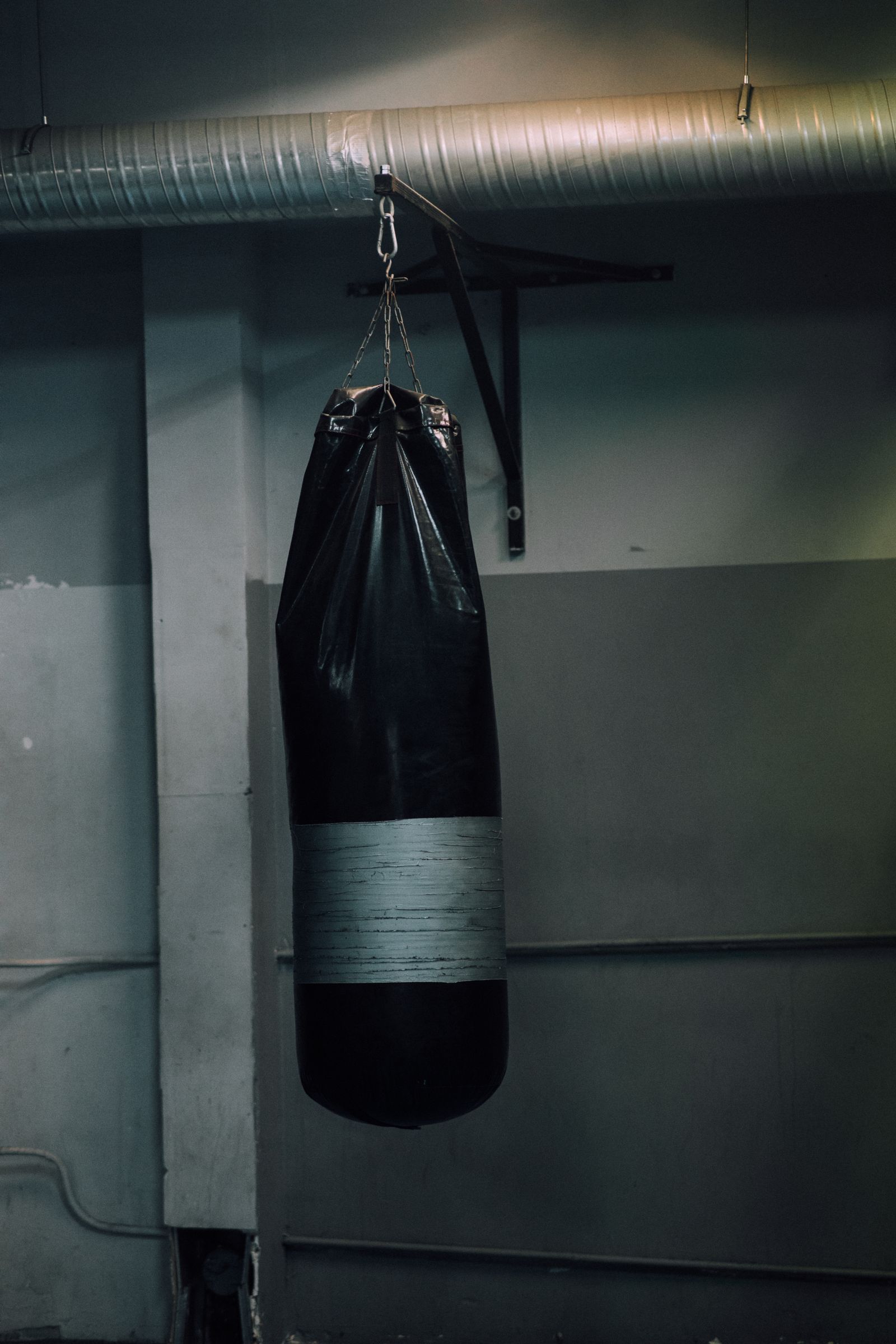 A heavy bag hanging from a chain in a quiet corner of the gym