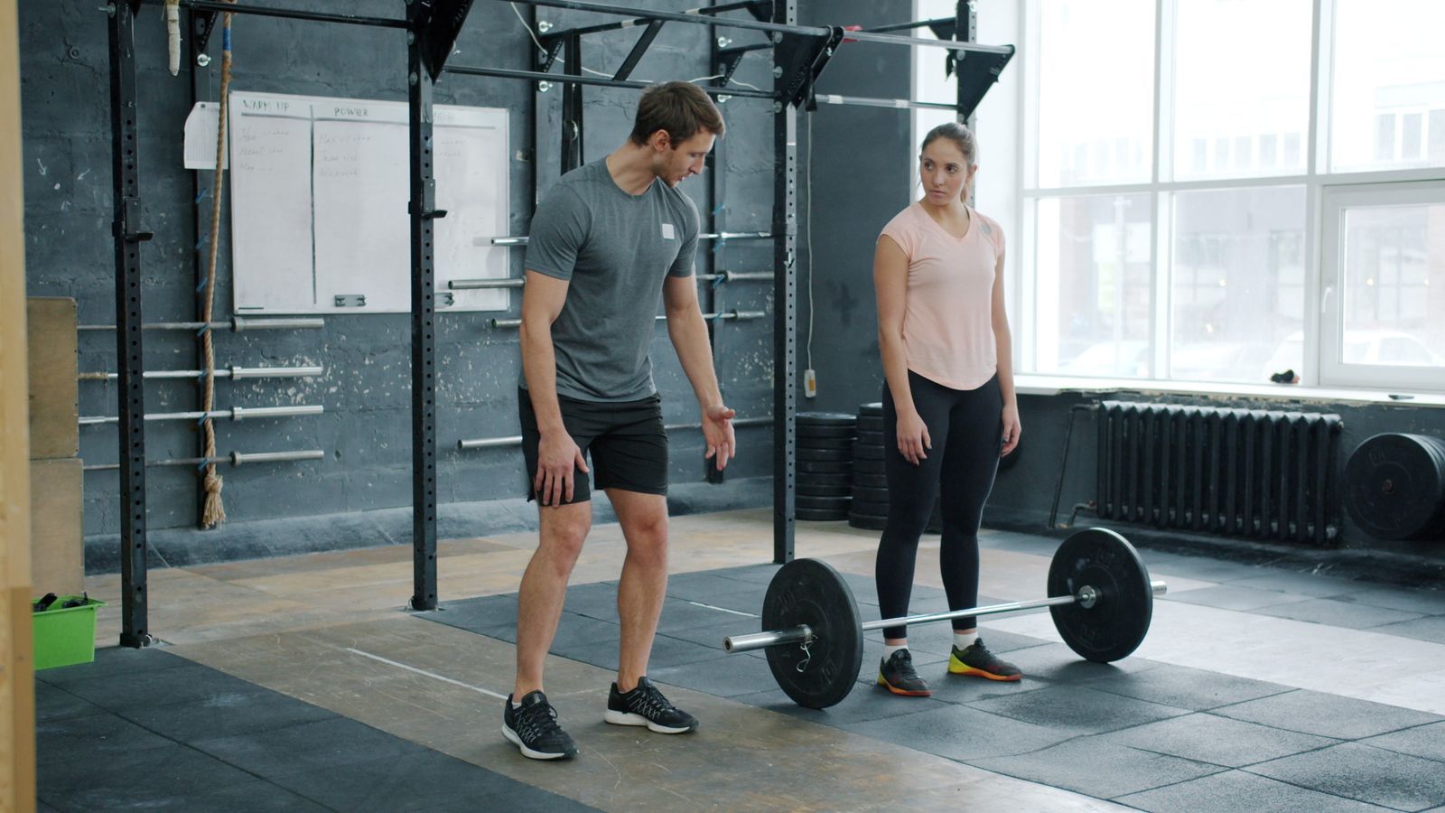A coach showing a client where to stand before a barbell deadlift