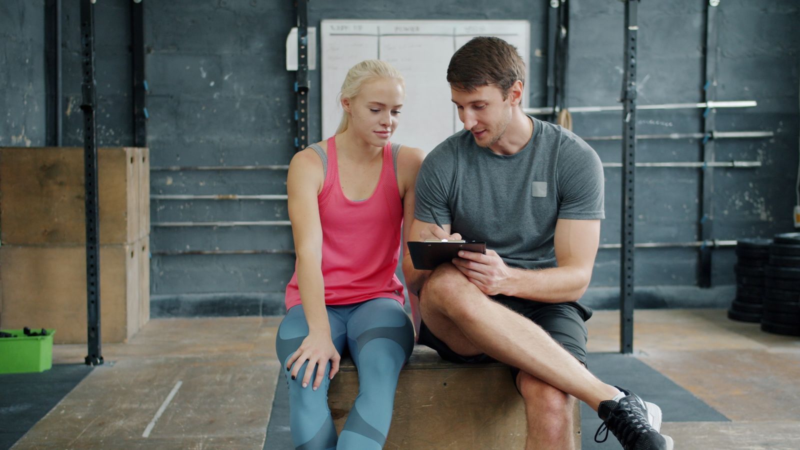 A coach and client sitting on a plyo box, reviewing notes between sets
