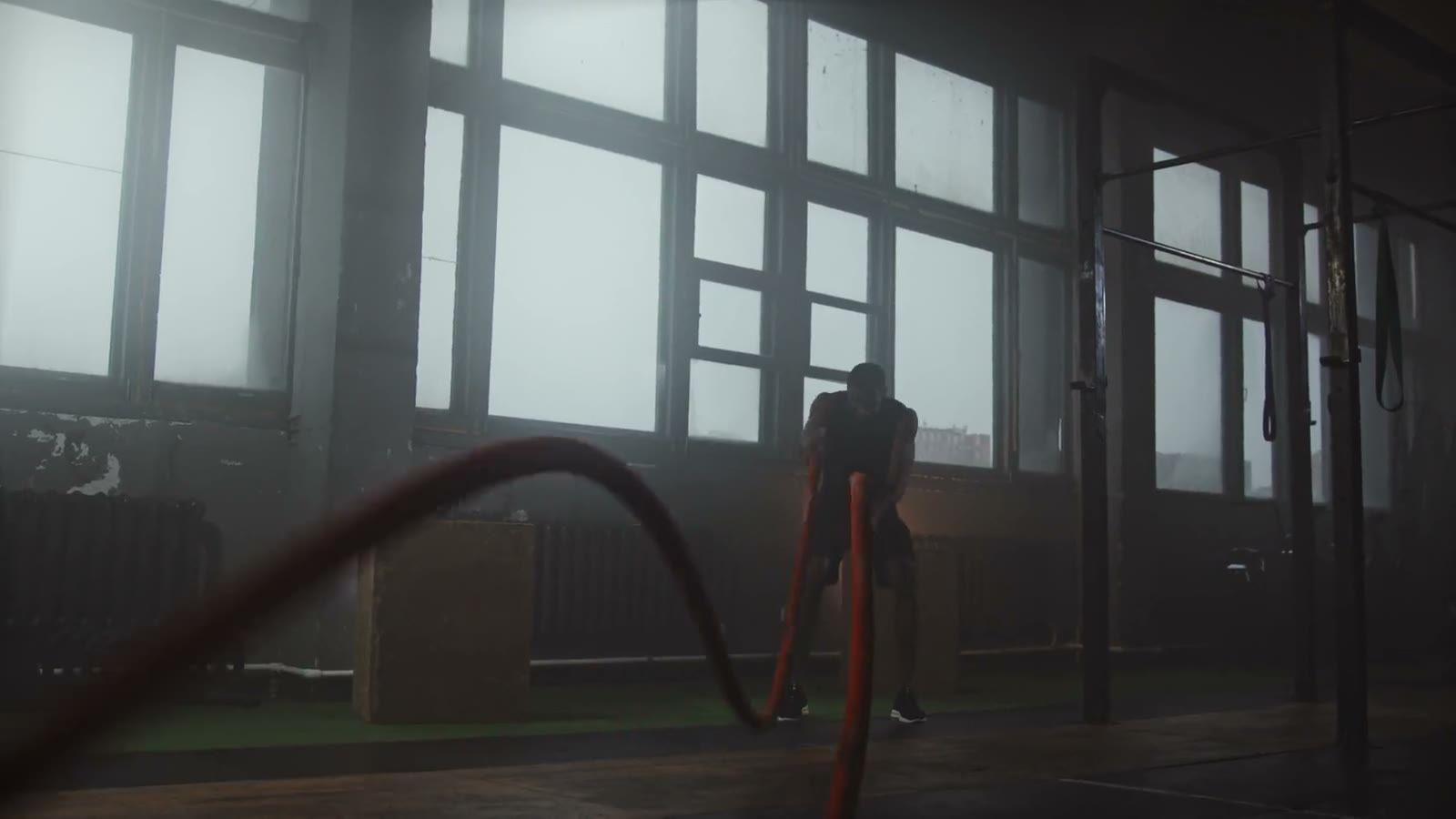 A member working battle ropes in a hazy warehouse gym