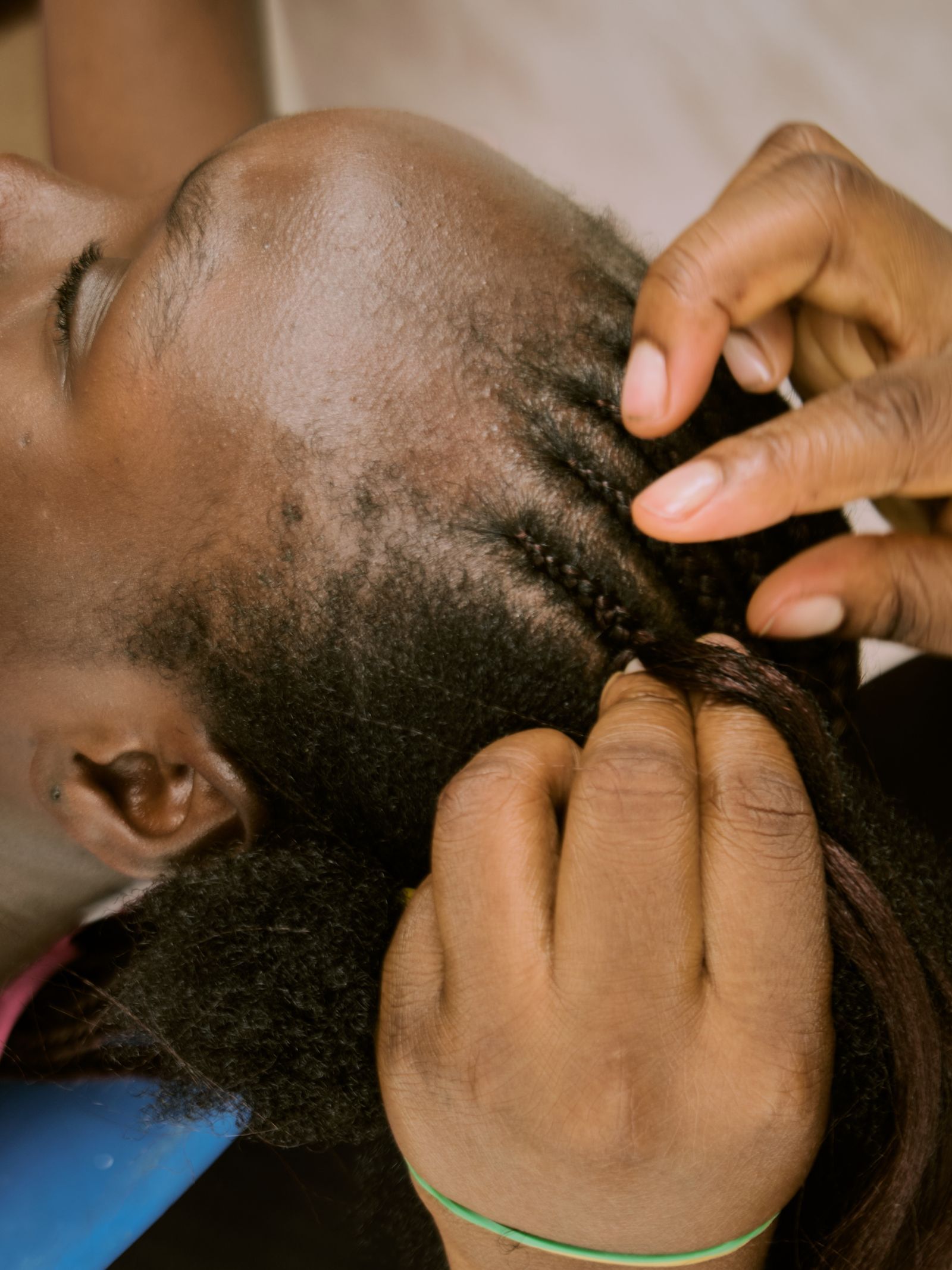 Close-up of hands sectioning and braiding hair close to the scalp