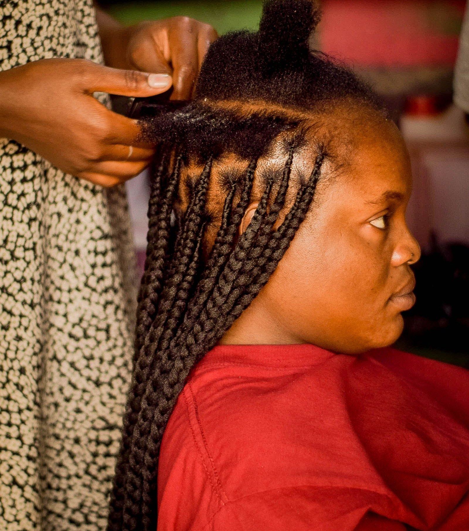 A braider adding extensions to a client's box braids in the salon