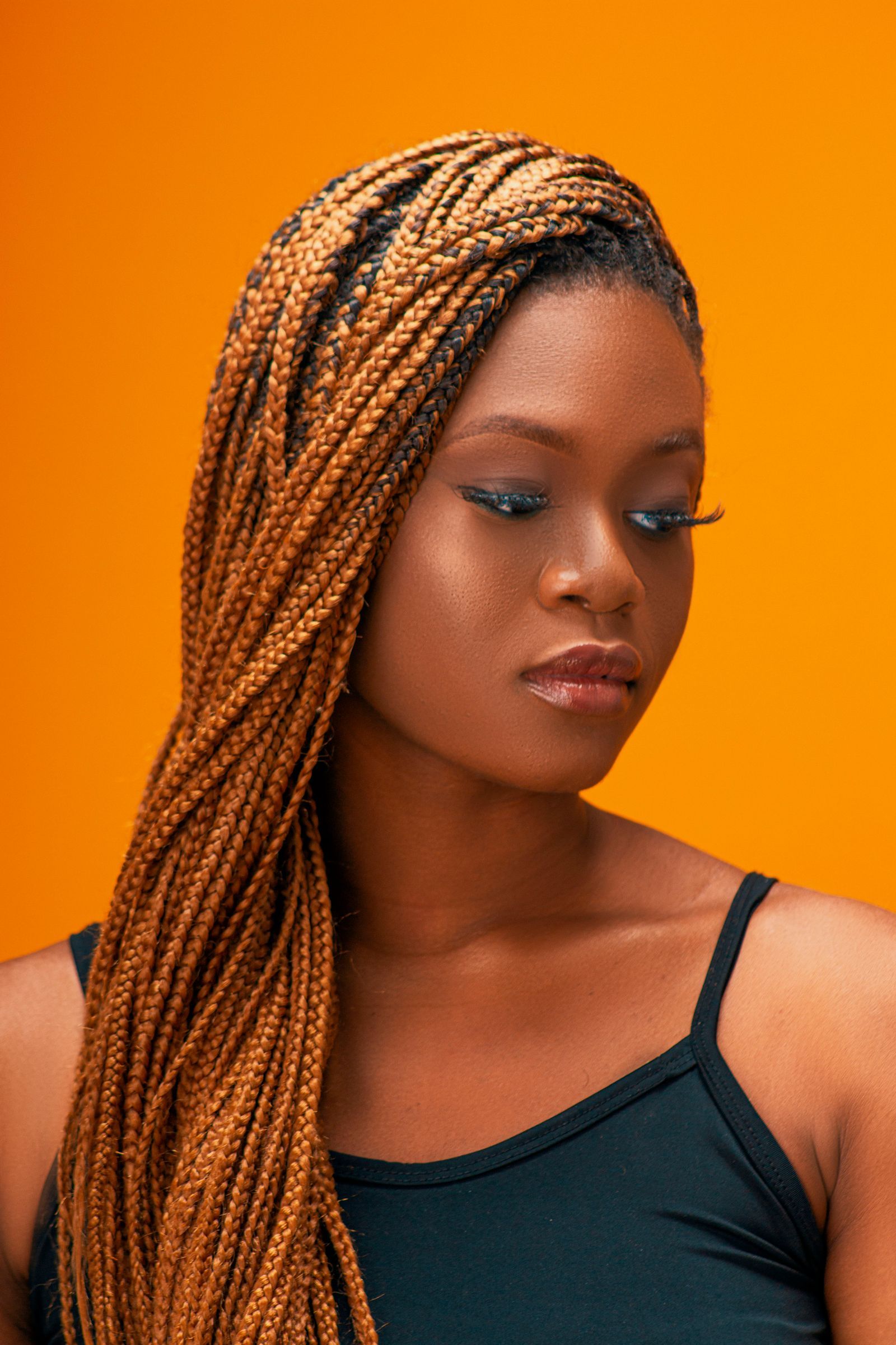 A woman with long honey-brown box braids against an orange wall