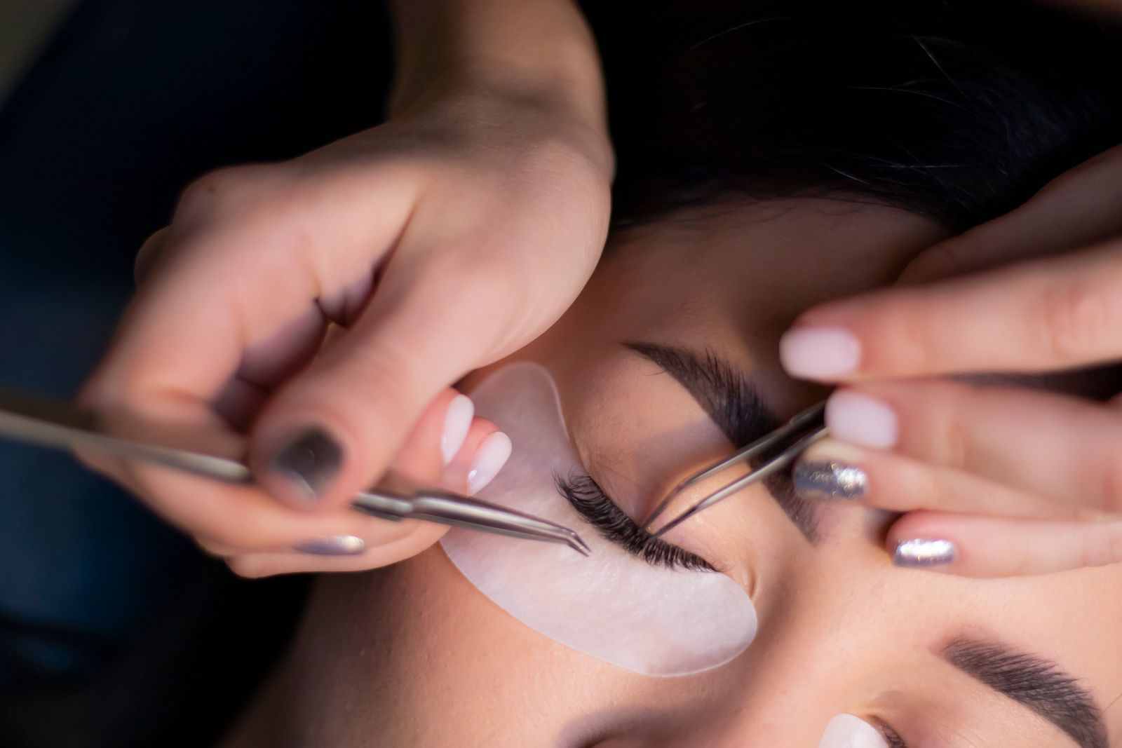 A lash artist placing extensions with fine tweezers while the client rests