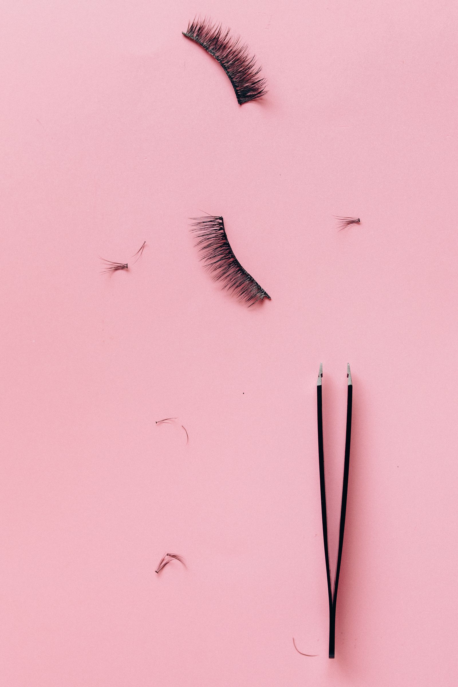 Loose false lashes and tweezers laid out on a pink surface