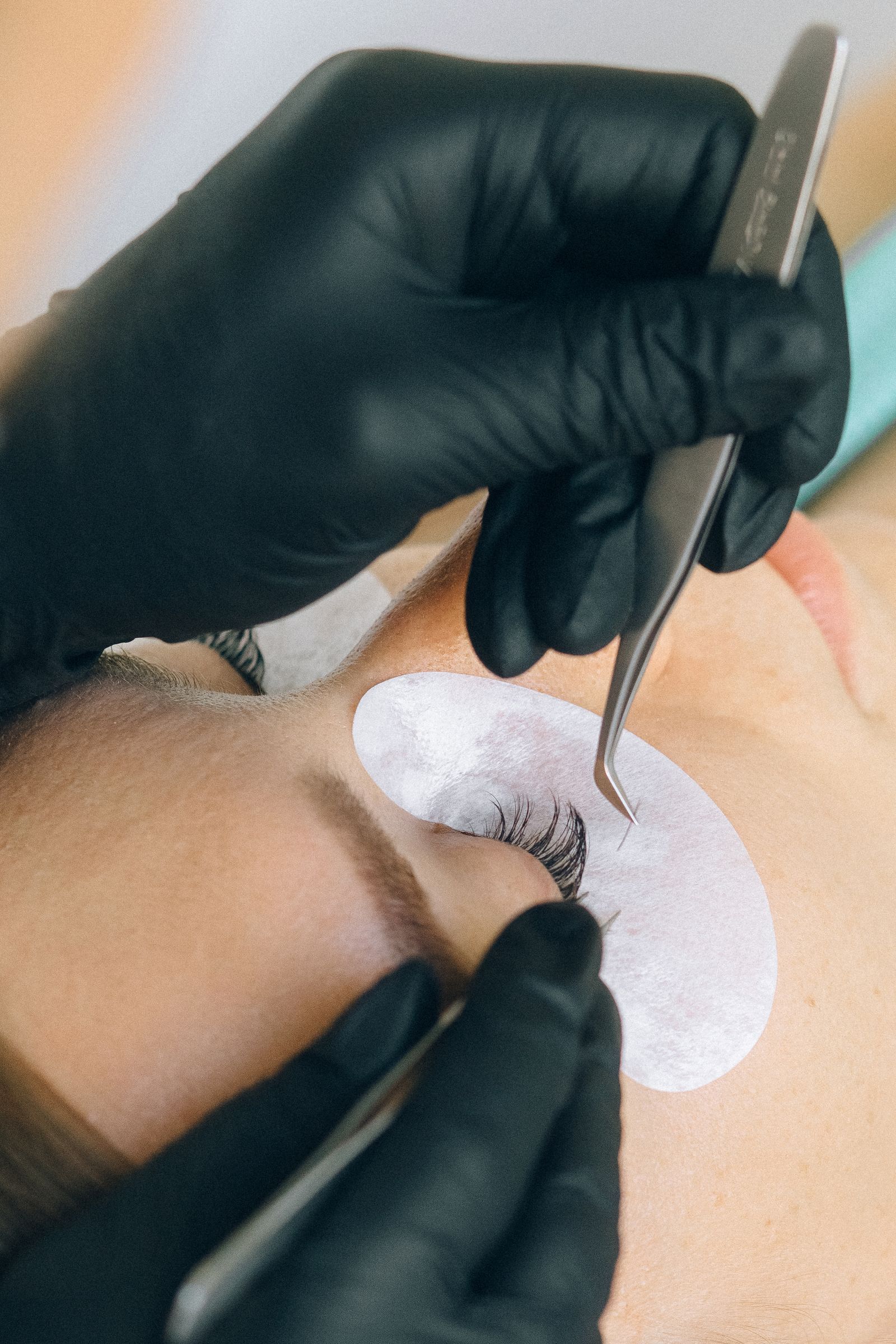 Gloved hands holding lash tweezers over an under-eye pad