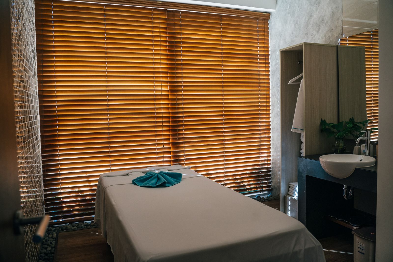 A dressed massage table in a quiet room with warm light through wooden blinds