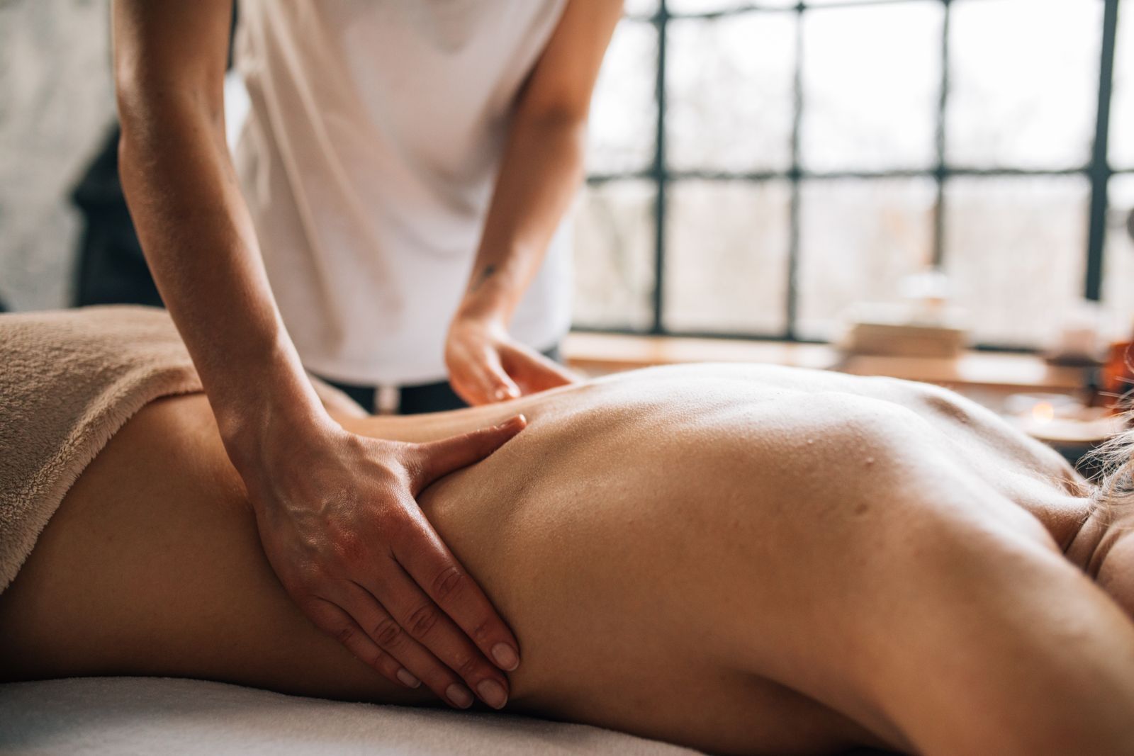 A practitioner giving a back massage in a softly lit room with a draped table