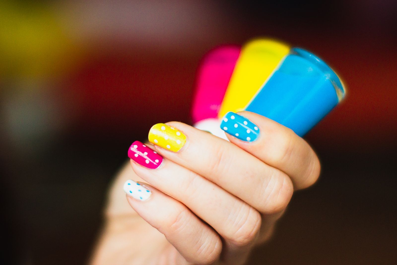 Short nails painted pink, yellow, blue, and white with contrasting polka dots