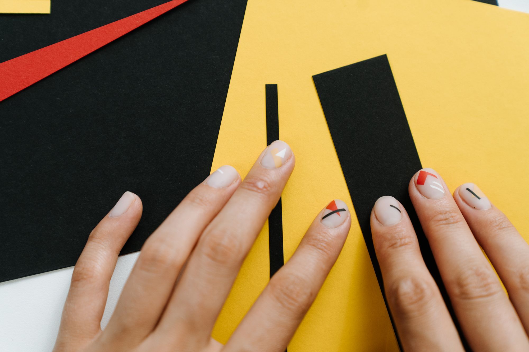 Short natural nails with small red, yellow, and black geometric shapes