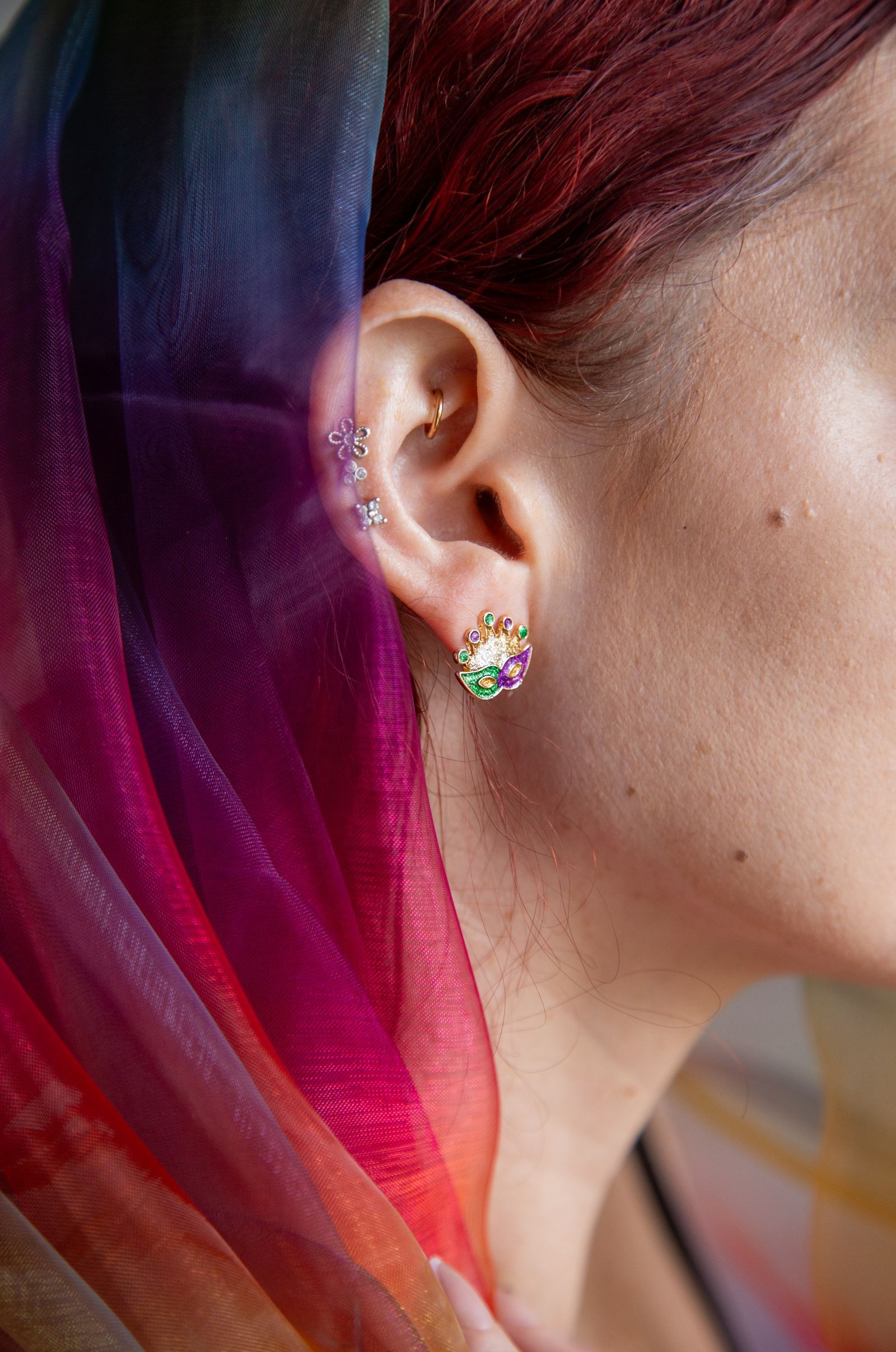 An ear with colourful stone studs next to bright hair