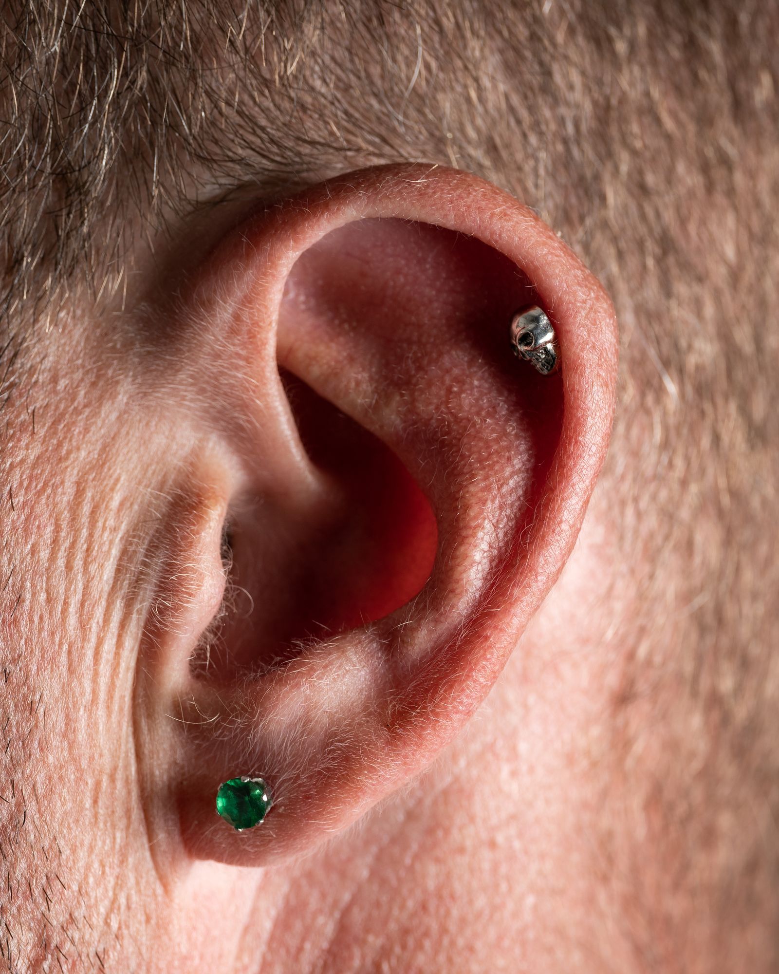 Close-up of an ear with a green stone stud in the lobe and a small gem in the helix