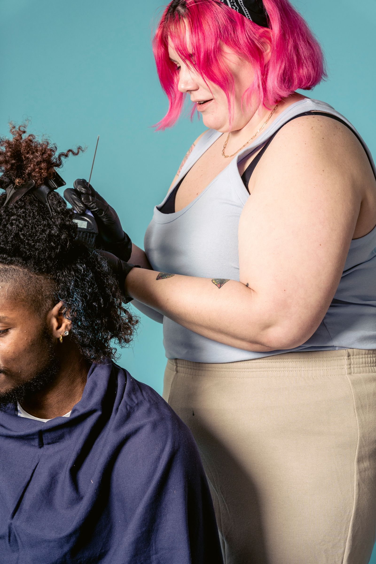 A stylist with bright pink hair working on a client's natural curls