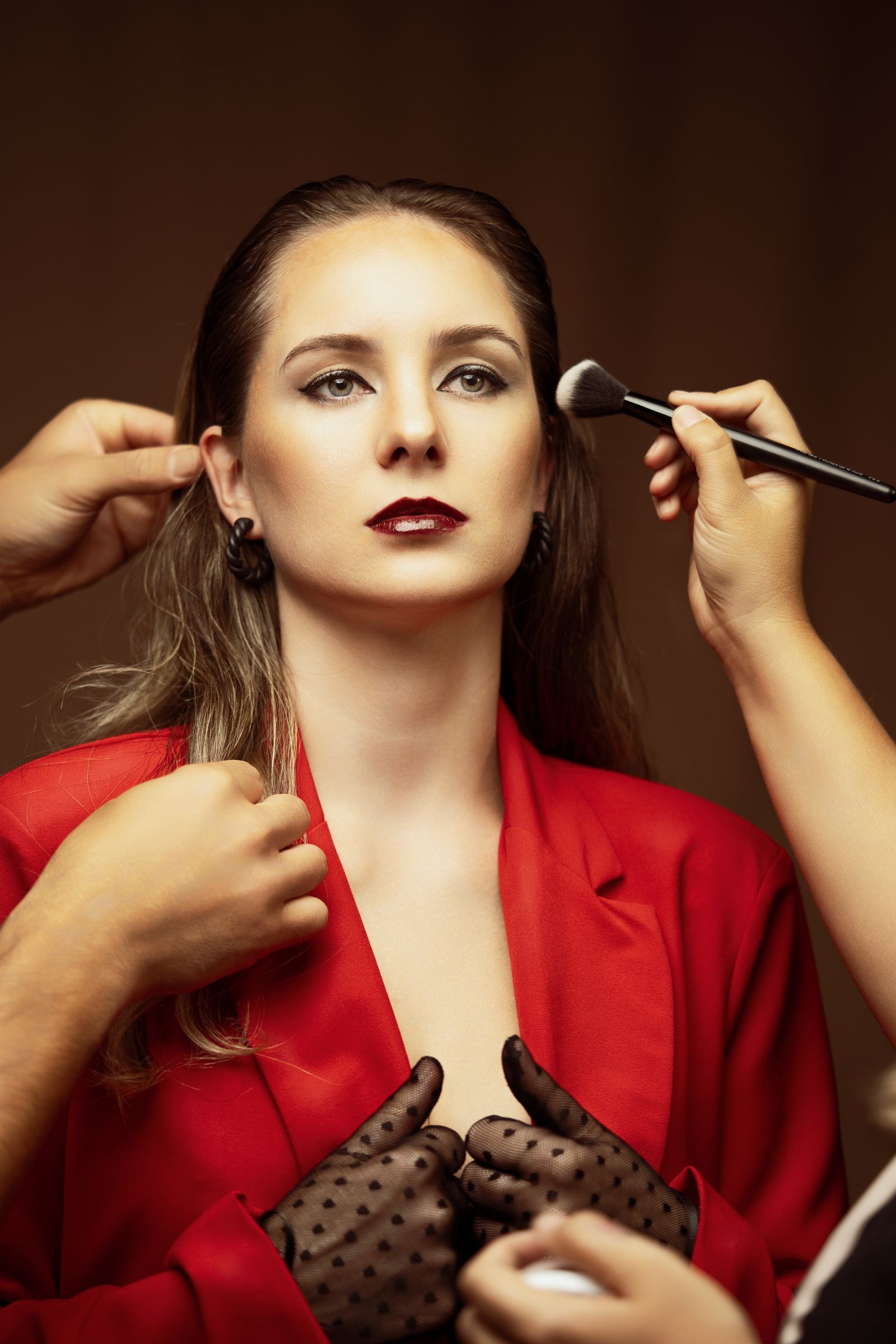 A woman in a red jacket having her hair and makeup finished for a shoot