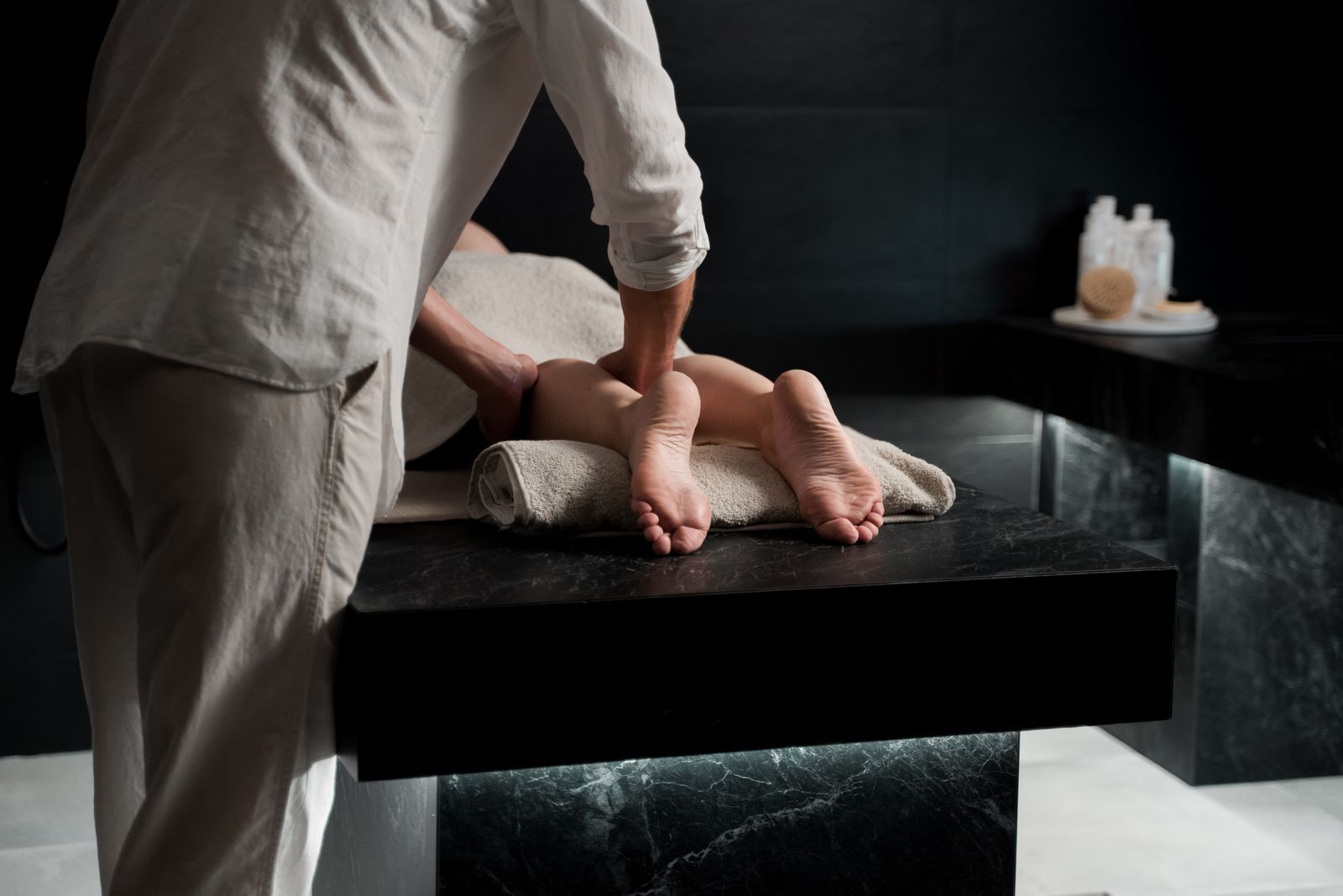 A practitioner working on a guest's feet on a black marble treatment table lit from below