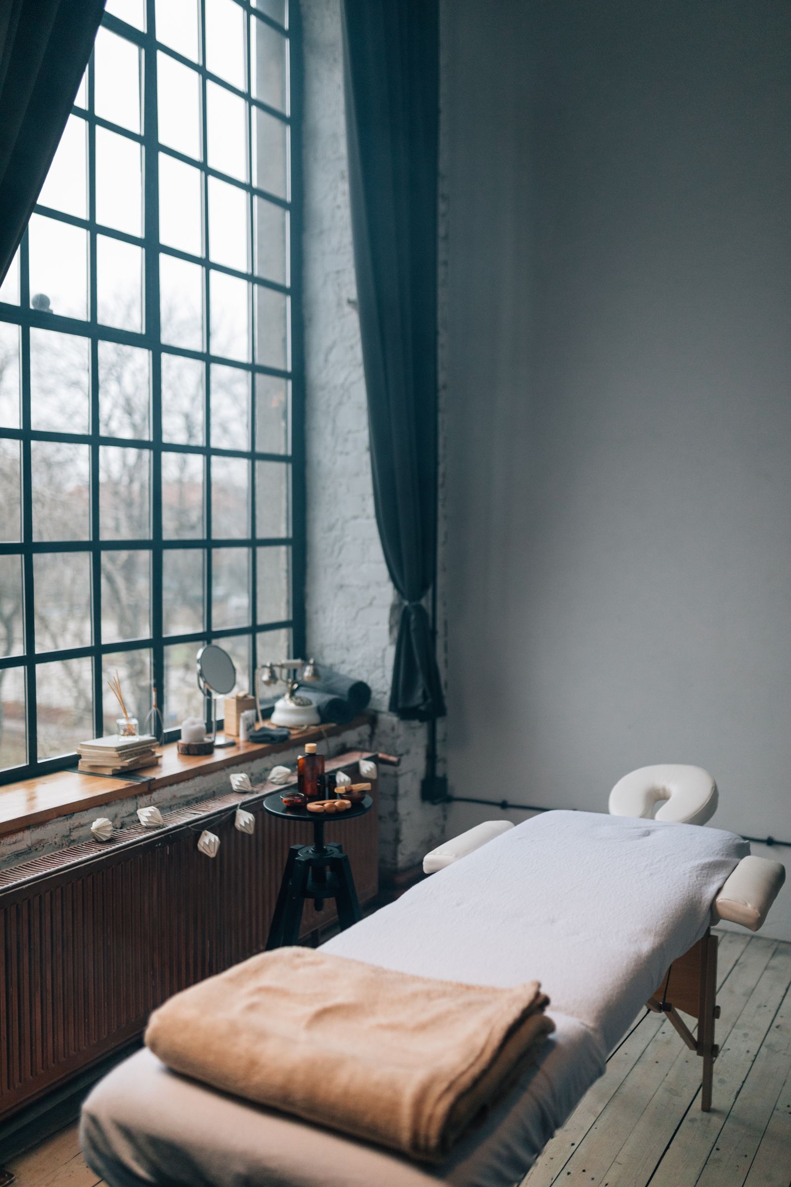A treatment room with a massage table in soft window light