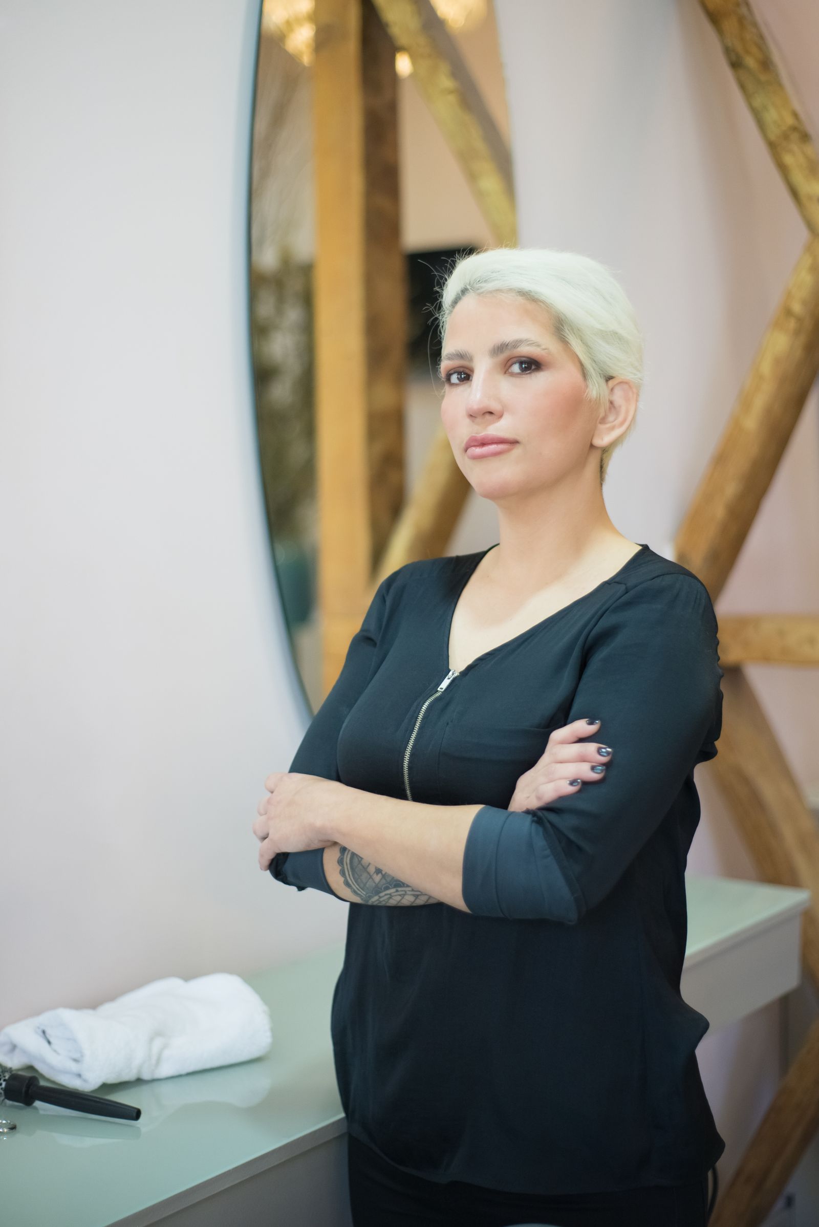 Sol Herrera with platinum hair, arms crossed, in front of a round mirror