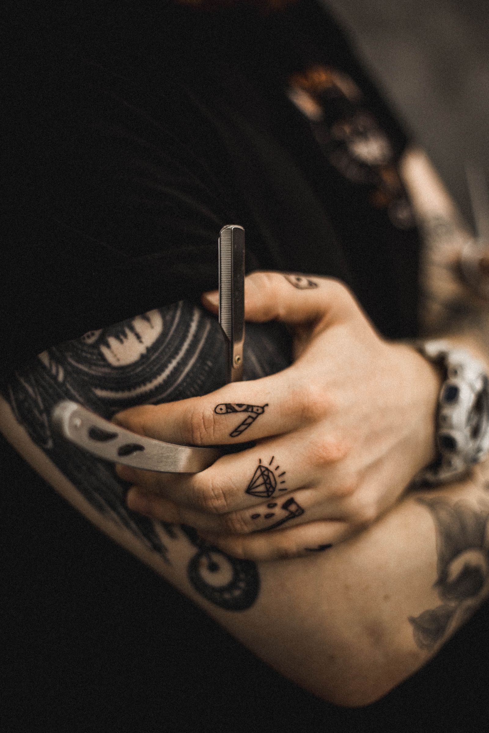A black and grey straight razor tattoo on a hand