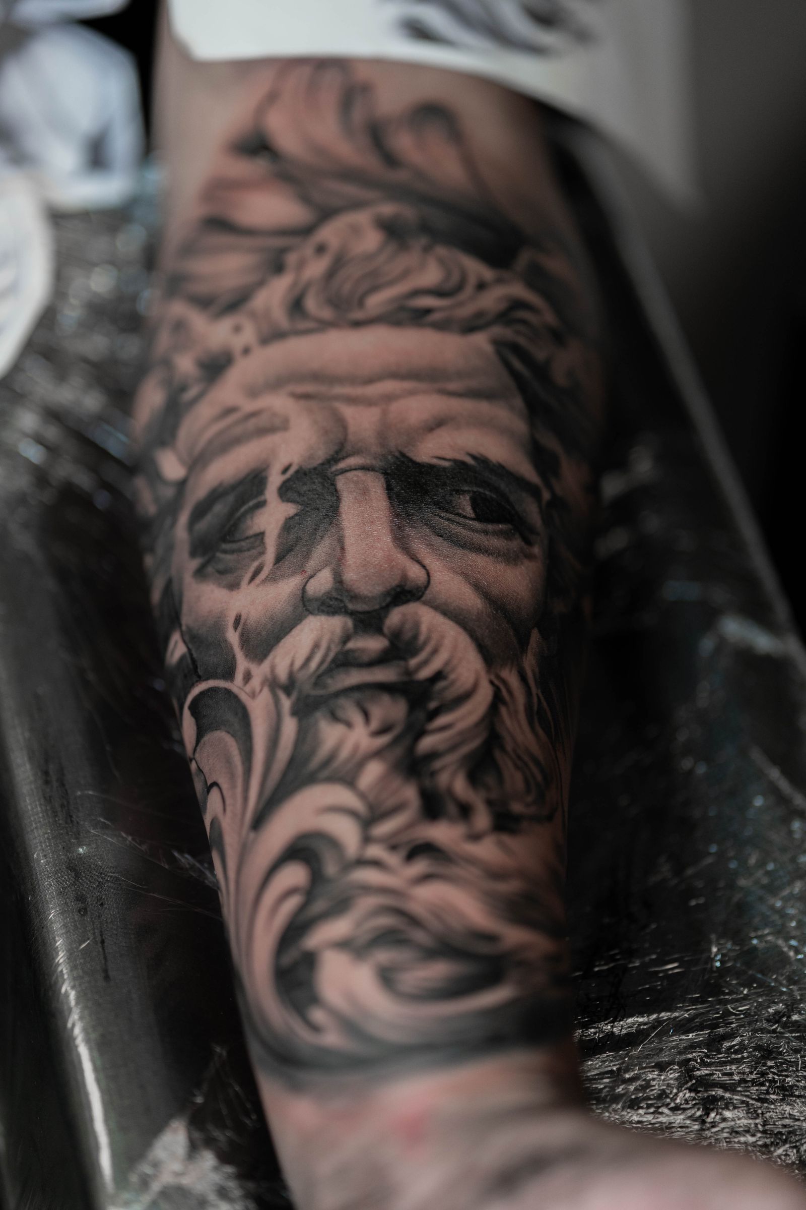 A black and grey statue tattoo on a forearm