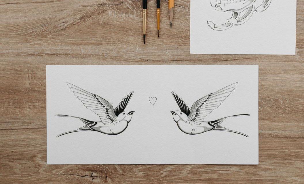 Black ink flash drawing of two swallows facing a small heart