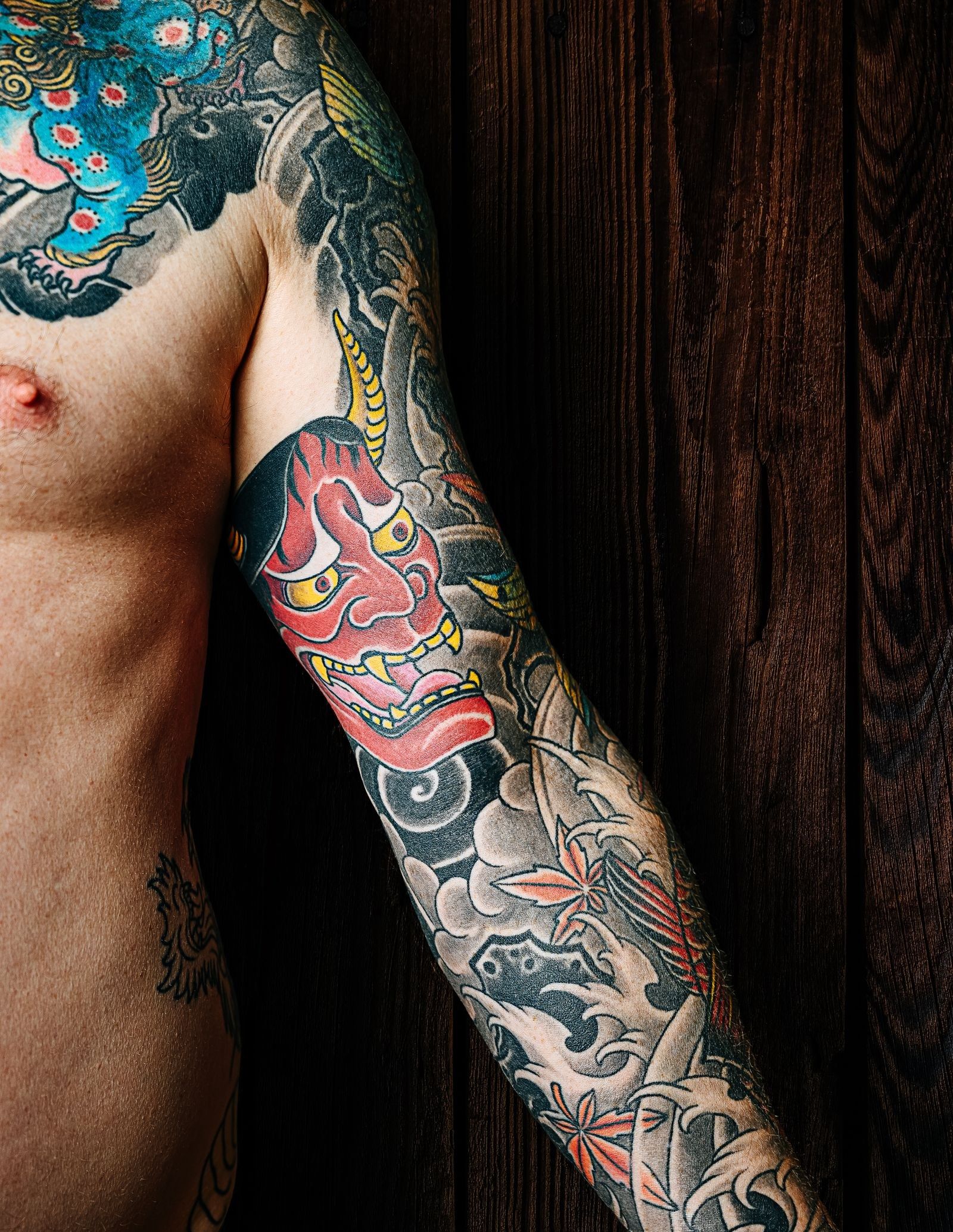 A full sleeve with a red hannya mask, waves, and maple leaves