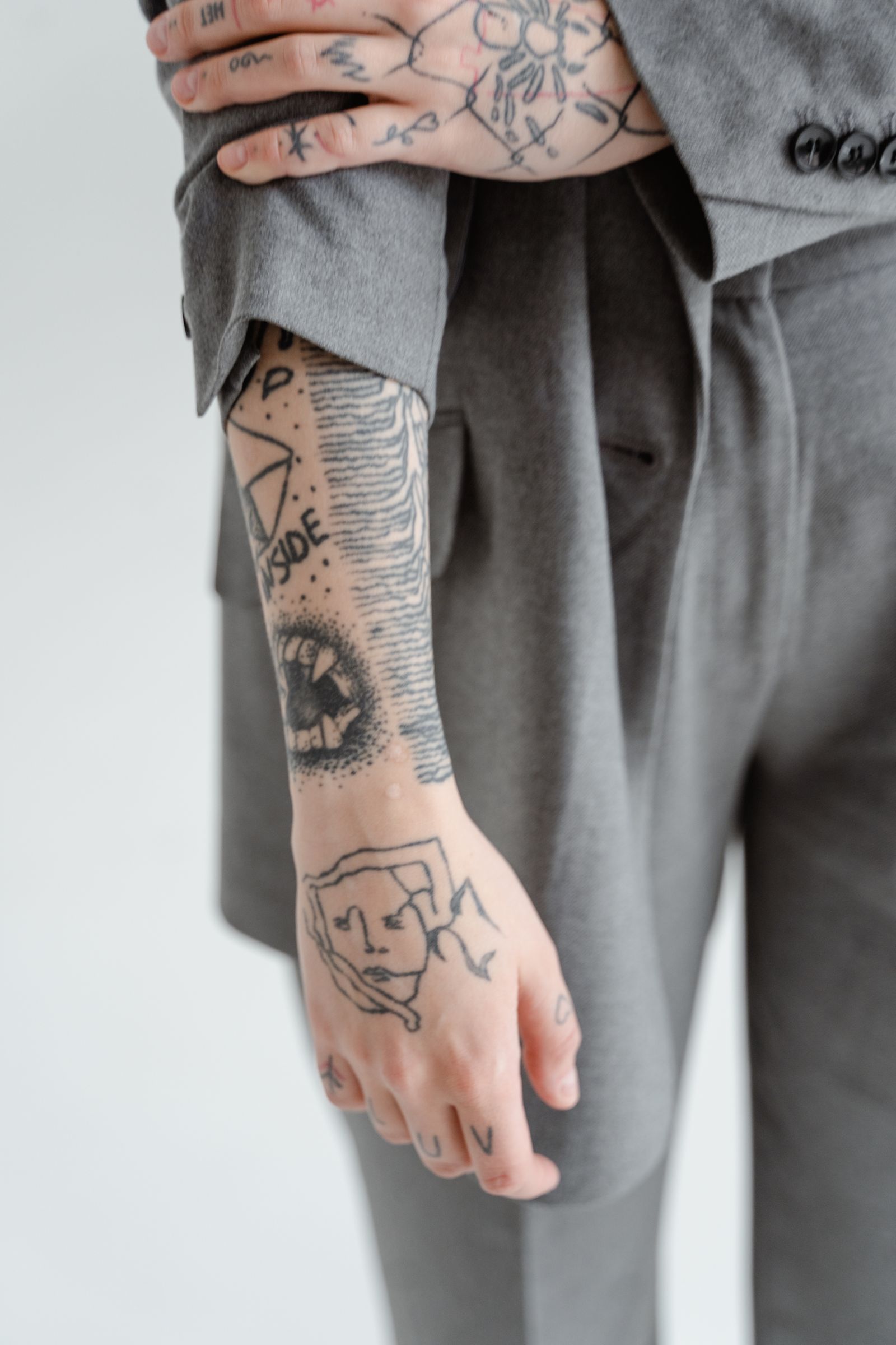 A heavily tattooed hand and wrist with small black designs, against a grey suit