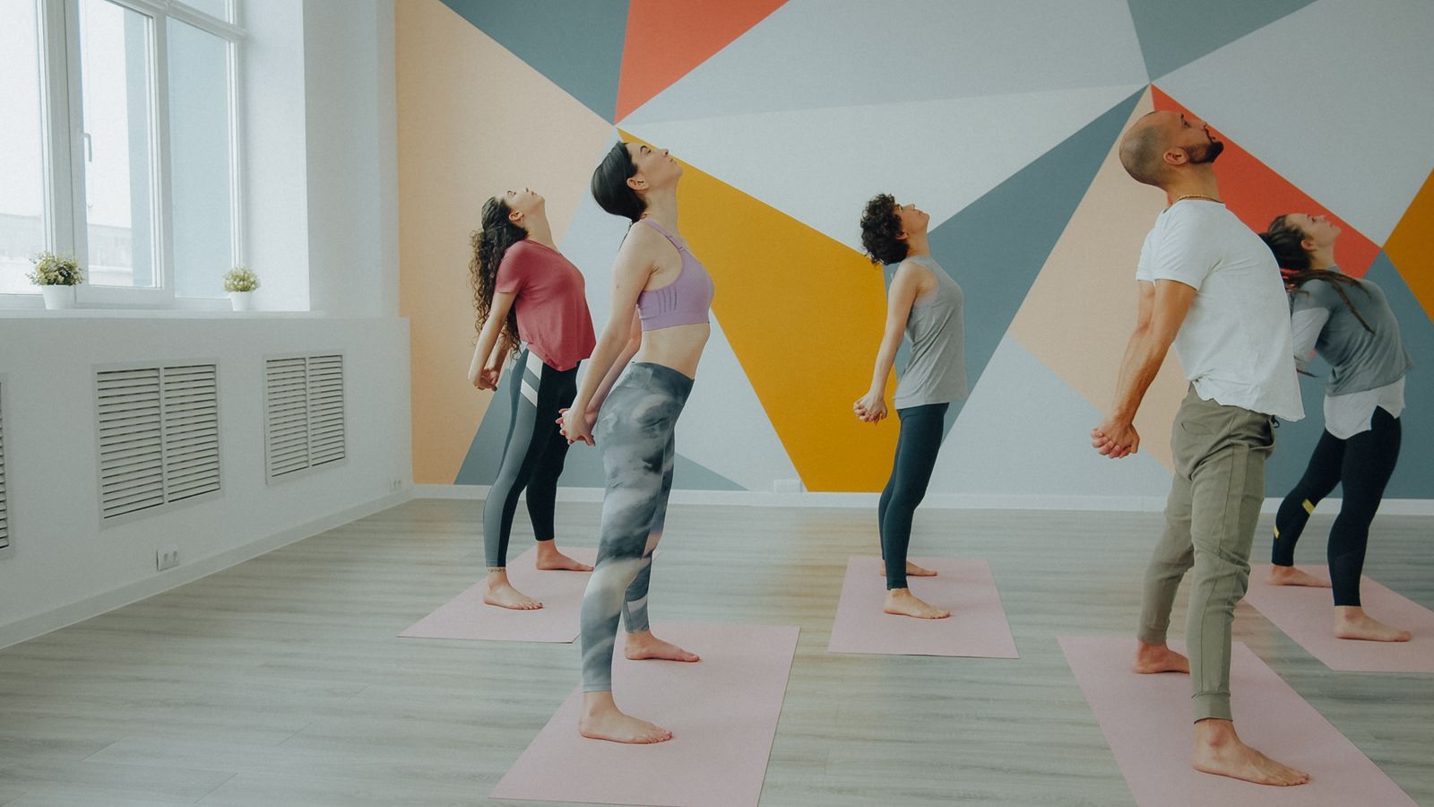 Students in a standing backbend in a studio with a painted geometric wall