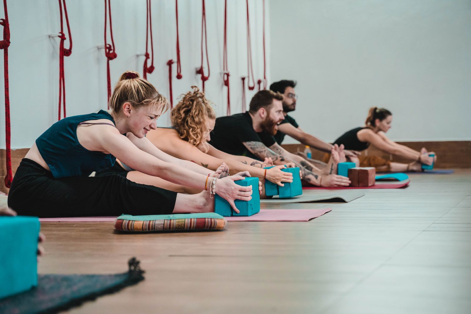 A row of students in a seated forward fold, holding yoga blocks